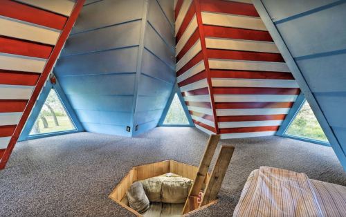Interior of a unique, colorful room with slanted walls, large windows, and a cozy seating area.