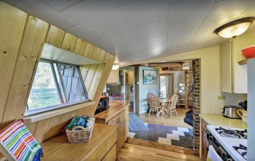 Cozy kitchen with wooden accents, a large window, and a view into a dining area with wicker chairs.