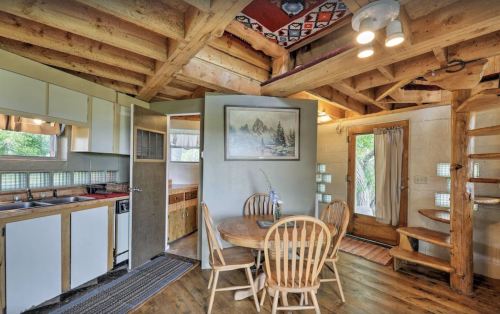 Cozy cabin interior featuring a kitchen, dining area with wooden table, and spiral staircase. Natural light fills the space.