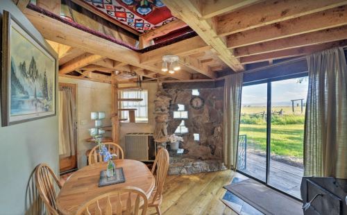 Cozy interior of a rustic cabin with wooden furniture, stone accents, and large windows overlooking a grassy landscape.