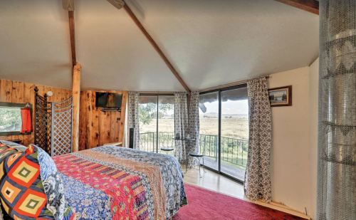 Cozy bedroom with colorful quilts, wooden walls, and large windows overlooking a scenic view.