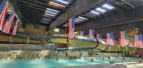 Indoor pool with a large water slide, surrounded by hanging American flags and people enjoying the water.