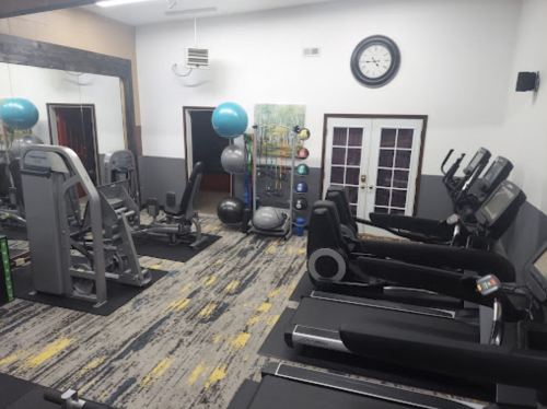 A gym interior featuring exercise machines, a clock, and fitness equipment against a mirrored wall.