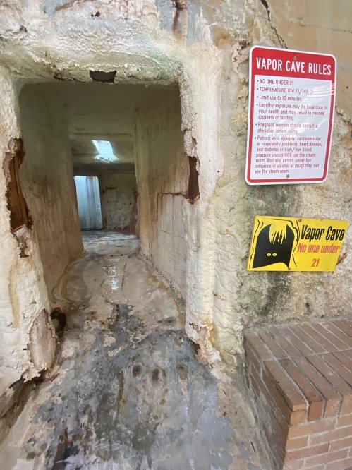 A dimly lit corridor with peeling walls, featuring signs about vapor cave rules and age restrictions.