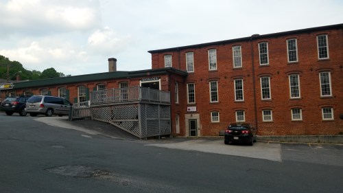 A brick building with multiple windows, a wooden deck, and parked cars on a sloped driveway.