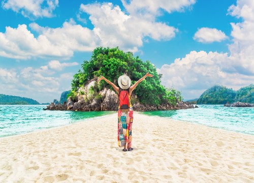 Woman enjoying a sunny day on the sandy beach of Pak Bia Island in Krabi, Thailand, surrounded by clear turquoise water and dramatic limestone cliffs.