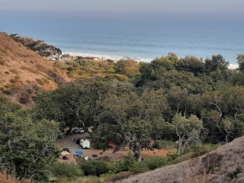 A scenic view of a campsite surrounded by trees, with the ocean visible in the background.