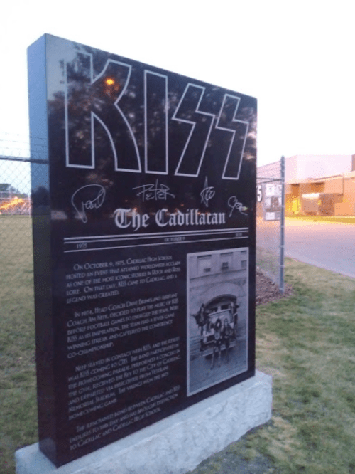 A black monument with "KISS" and "The Cadillacan" inscribed, featuring signatures and historical details about the band.