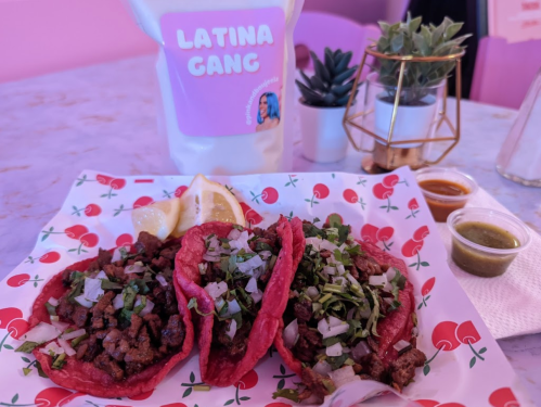 Three vibrant red tacos filled with beef, onions, and cilantro, served with lemon and sauces on a colorful plate.