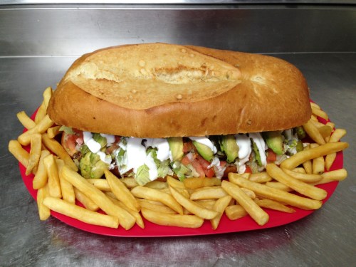 A large sandwich filled with vegetables and sauces, served with a side of golden French fries on a red plate.