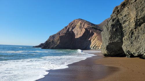 A serene beach scene with gentle waves, rocky cliffs, and clear blue skies.