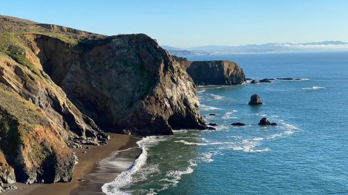 A scenic coastal view featuring cliffs, a sandy beach, and calm blue waters under a clear sky.