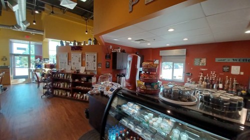 Cozy café interior with a display case, shelves of products, and colorful walls, featuring seating and large windows.