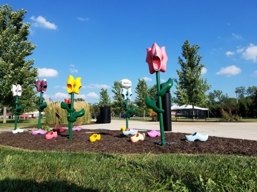 Colorful flower sculptures in a park, surrounded by green grass and trees under a clear blue sky.
