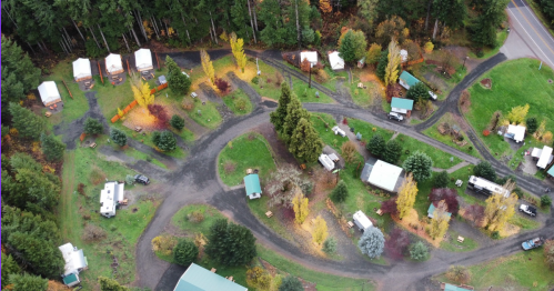 Aerial view of a campground with cabins, RVs, and trees, surrounded by autumn foliage and a nearby road.