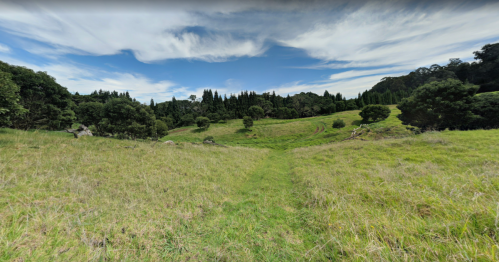 A grassy path leads through a lush, green landscape with trees and a blue sky dotted with clouds.