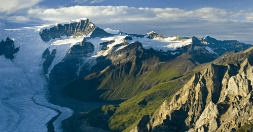 A stunning mountain landscape featuring glaciers, rugged peaks, and lush green valleys under a blue sky.
