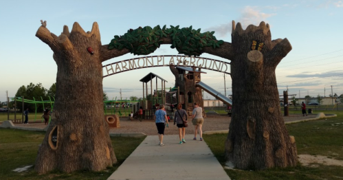 Entrance to Harmon Playground featuring large tree sculptures and children playing in the background.