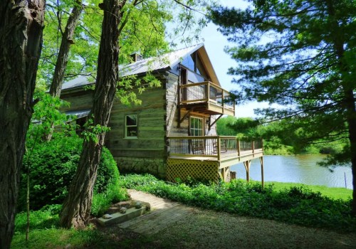 A rustic wooden cabin with a balcony, surrounded by greenery and overlooking a serene pond.