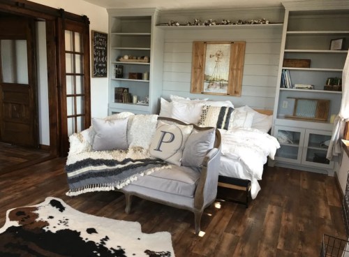 Cozy bedroom with a sofa, bed, and rustic decor, featuring wooden shelves and a cowhide rug on the floor.