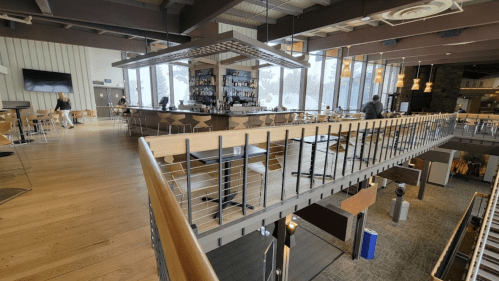A spacious, modern restaurant interior with a bar, large windows, and wooden accents.