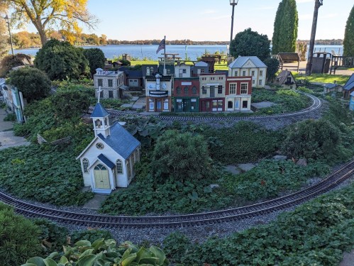 A miniature village with colorful buildings and a church, surrounded by greenery and a train track near a lake.