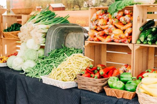 A vibrant display of fresh vegetables in wooden crates, including peppers, beans, and leafy greens at a market.