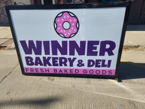 Sign for Winner Bakery & Deli featuring a donut graphic and text promoting fresh baked goods.