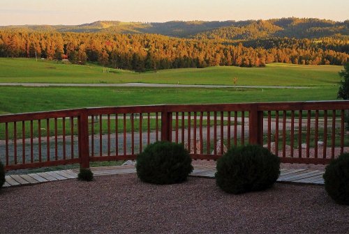 A scenic view of rolling green hills and trees under a golden sunset, seen from a wooden deck.