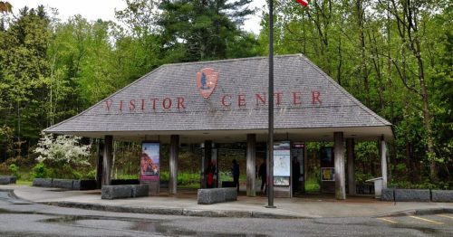A visitor center with a sloped roof, surrounded by greenery, featuring a sign that reads "Visitor Center."