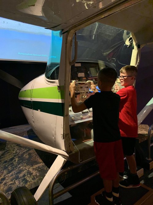 Two children interact with a flight simulator inside a small aircraft exhibit at a museum.