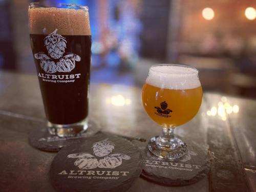 Two glasses of beer on a bar: a dark stout in a tall glass and a light ale in a short glass, both with logo coasters.