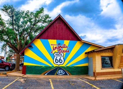Colorful mural of Route 66 on a building in Amarillo, Texas, with a bright sunburst design and welcoming text.