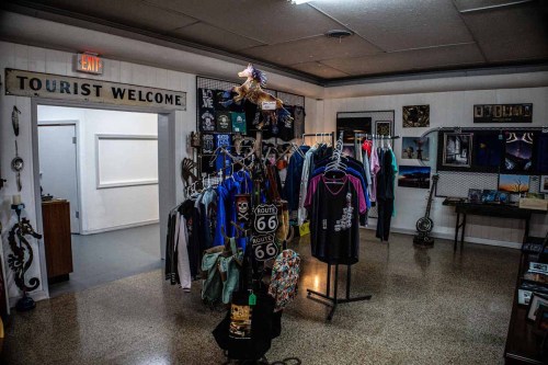 A gift shop interior with clothing racks, souvenirs, and a "Tourist Welcome" sign on the wall.