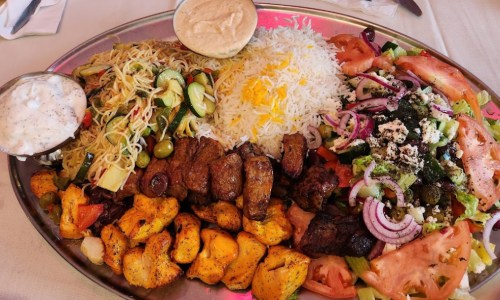 A large platter featuring grilled meats, rice, salad, vegetables, and sauces, beautifully arranged.