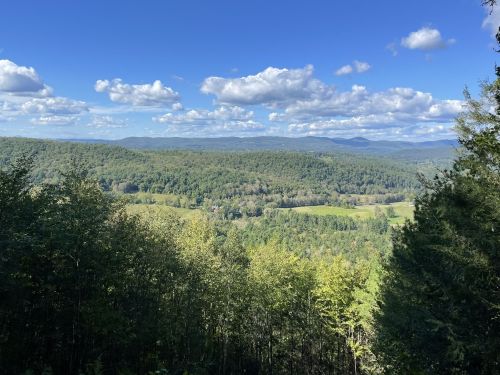 A panoramic view of lush green mountains and valleys under a blue sky with fluffy white clouds.