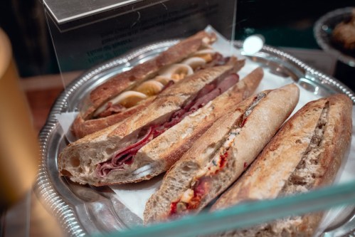 A close-up of three gourmet sandwiches on a silver platter, featuring various fillings in crusty bread.