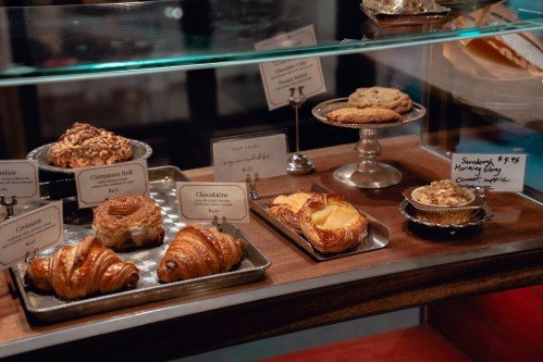 A display case filled with various pastries, including croissants, cinnamon rolls, and cookies, with price tags.