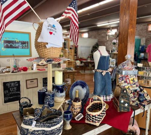 A display of decorative items, including baskets, dishware, and a towel, with American flags in a market setting.