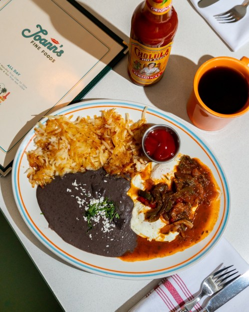 A plate of breakfast featuring eggs, black beans, hash browns, and a side of salsa, with a coffee cup and menu in the background.