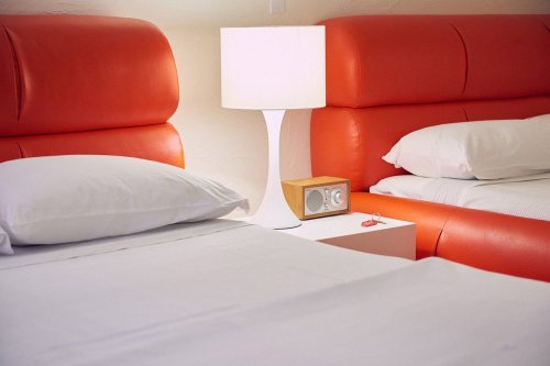 Two orange upholstered beds with white pillows, a bedside table, a lamp, and a vintage radio.