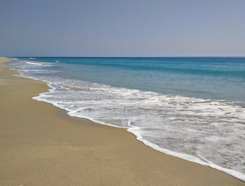A serene beach scene with gentle waves lapping at the sandy shore under a clear blue sky.