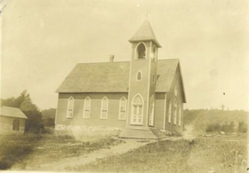 Historic church building with a tall steeple, arched windows, and a grassy area in front, captured in sepia tones.