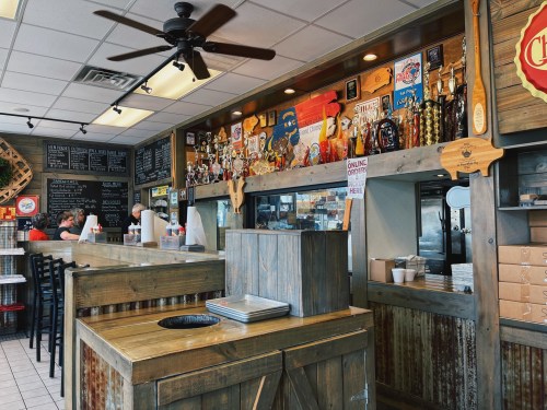 A cozy restaurant interior with wooden decor, a counter, and walls adorned with memorabilia and menu boards.