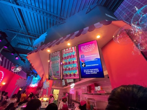 Colorful interior of a dessert shop with a menu board and vibrant decor, featuring people enjoying their treats.