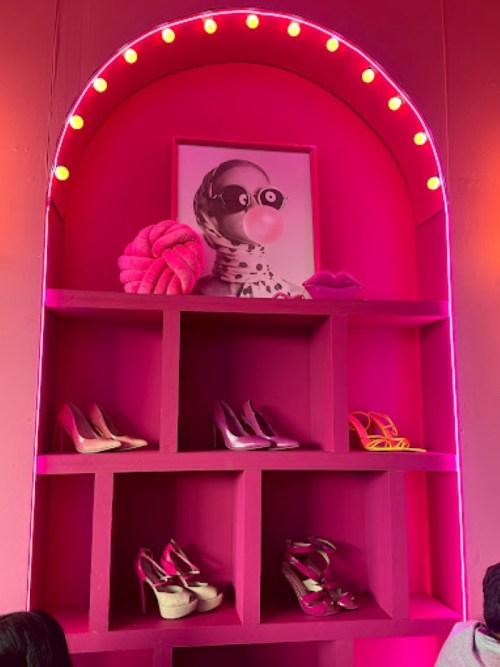 A vibrant pink display featuring stylish shoes on shelves, with a playful art piece above.