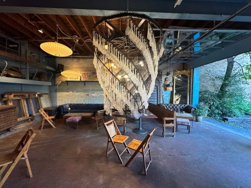 A stylish interior featuring a large chandelier, wooden furniture, and a cozy atmosphere with natural light.