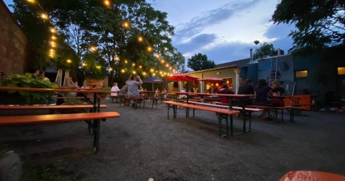 A cozy outdoor dining area with string lights, tables, and people enjoying the evening atmosphere.