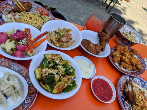 A colorful spread of various dishes, including noodles, fried chicken, dumplings, and fresh vegetables on a vibrant table.
