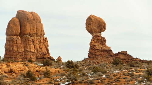 Two large rock formations in a desert landscape, one resembling a head and the other a tall, rounded structure.